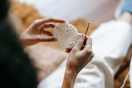 From above of crop anonymous female artisan with hook and crocheted fabric sitting in house room